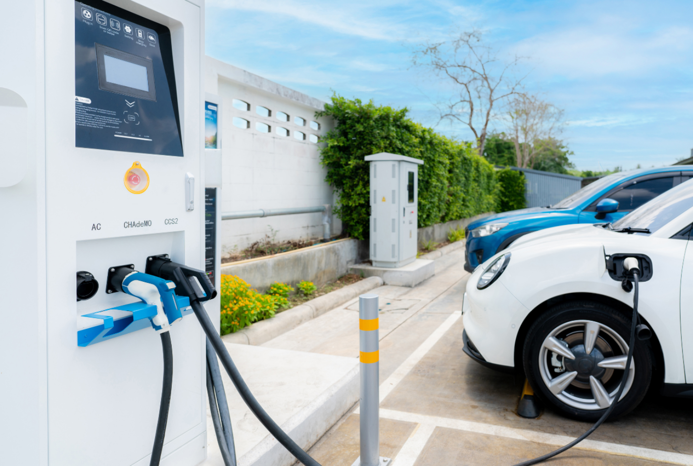 Des voitures électriques sont garées et rechargées à une station de recharge en plein air, avec deux connecteurs de recharge visibles branchés sur les véhicules.